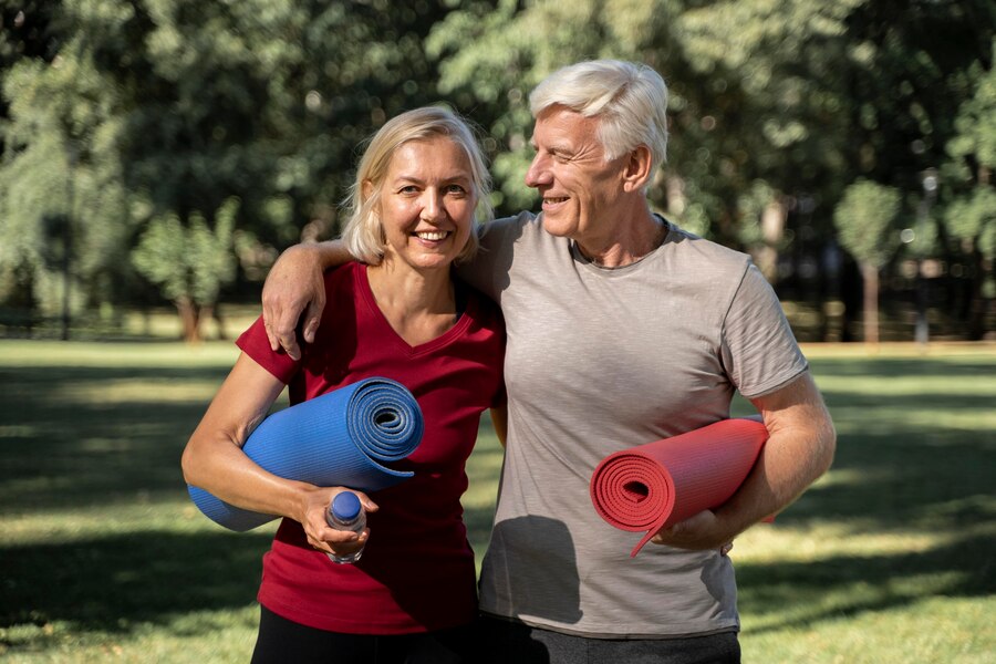 couple-personnes-agees-smiley-exterieur-tapis-yoga-bouteille-eau_23-2148729885